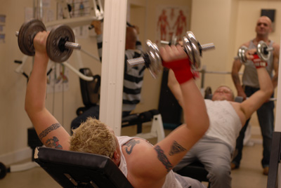 A blond man with tatoos lying on a training bench lifting weigths